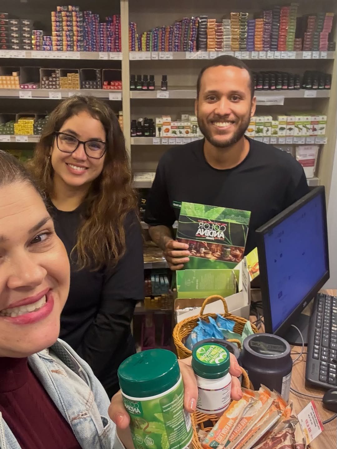 Marcela Nicacio no caixa de uma loja, equipe e gôndola de produtos ao fundo